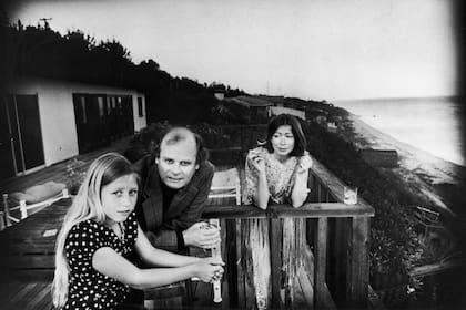 En una terraza con vista al mar en Malibú, Quintana Roo Dunne (izq.) se apoya en una baranda con sus padres, los autores y guionistas estadounidenses John Gregory y Joan Didion